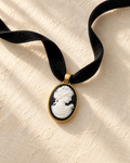 Noir Muse black velvet cameo collar photographed on a warm ivory textured background.