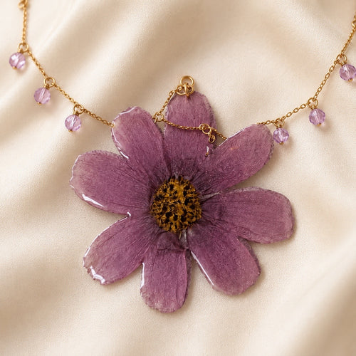 Close-up of purple preserved flower pendant with gold chain and crystal drops